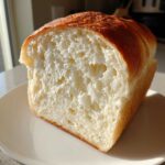 Close-up of a freshly baked japanese milk bread loaf showing its incredibly soft, white, and fluffy interior crumb structure.