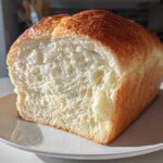 A close-up of a freshly baked loaf of japanese milk bread, showing its incredibly soft, white interior and golden brown top.