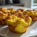 Close-up of several fluffy muffin tin egg bites with golden brown tops on a white plate.