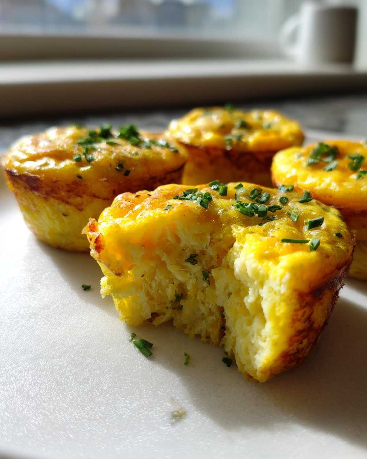 Close-up of fluffy muffin tin egg bites, one with a bite taken out, sprinkled with fresh chives.