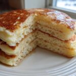 A stack of incredibly fluffy pancakes cut in half, showing their airy interior and golden tops drizzled with syrup.