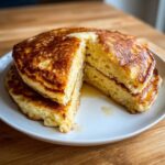 A stack of thick, golden-brown sourdough pancakes cut open to show the fluffy interior, topped with melting butter and syrup.