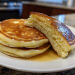 A stack of three fluffy sourdough pancakes drizzled with syrup, with one pancake cut open to show the airy interior.
