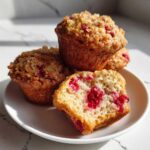 Close-up of fluffy strawberry muffins, one cut in half showing bright red fruit inside.
