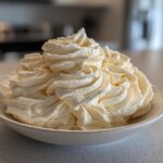 A large mound of perfectly piped, creamy vanilla buttercream frosting swirls filling a white bowl.
