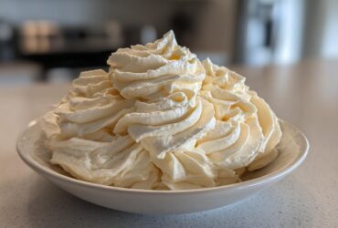 A large mound of perfectly piped, creamy vanilla buttercream frosting swirls filling a white bowl.