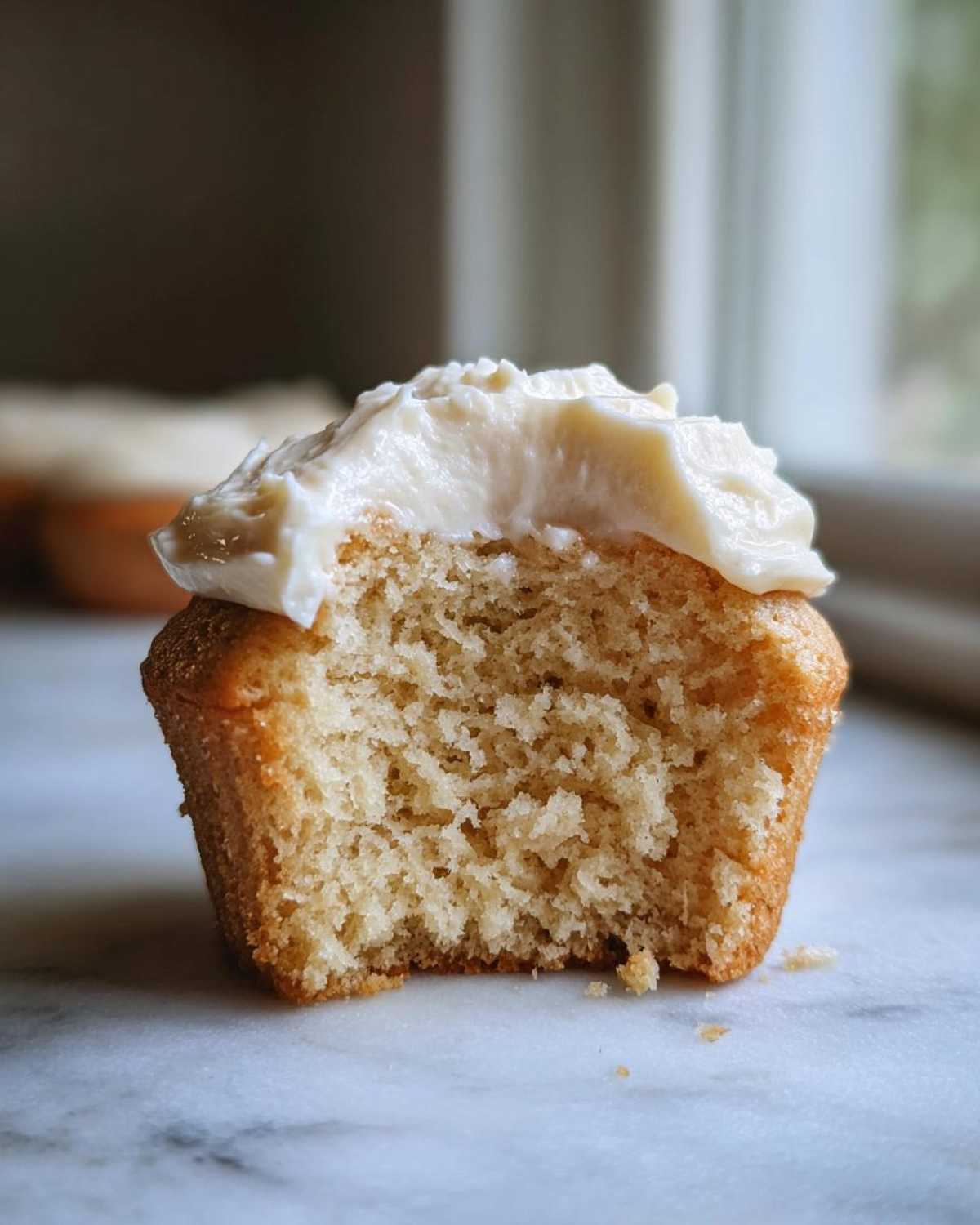 Close-up of a vanilla cupcake cut in half showing the fluffy interior and topped with white vanilla frosting.