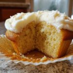 Close-up of a fluffy vanilla cupcake cut in half, showing the moist crumb and thick vanilla frosting.