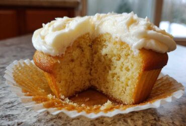 Close-up of a fluffy vanilla cupcake cut in half, showing the moist crumb and thick vanilla frosting.