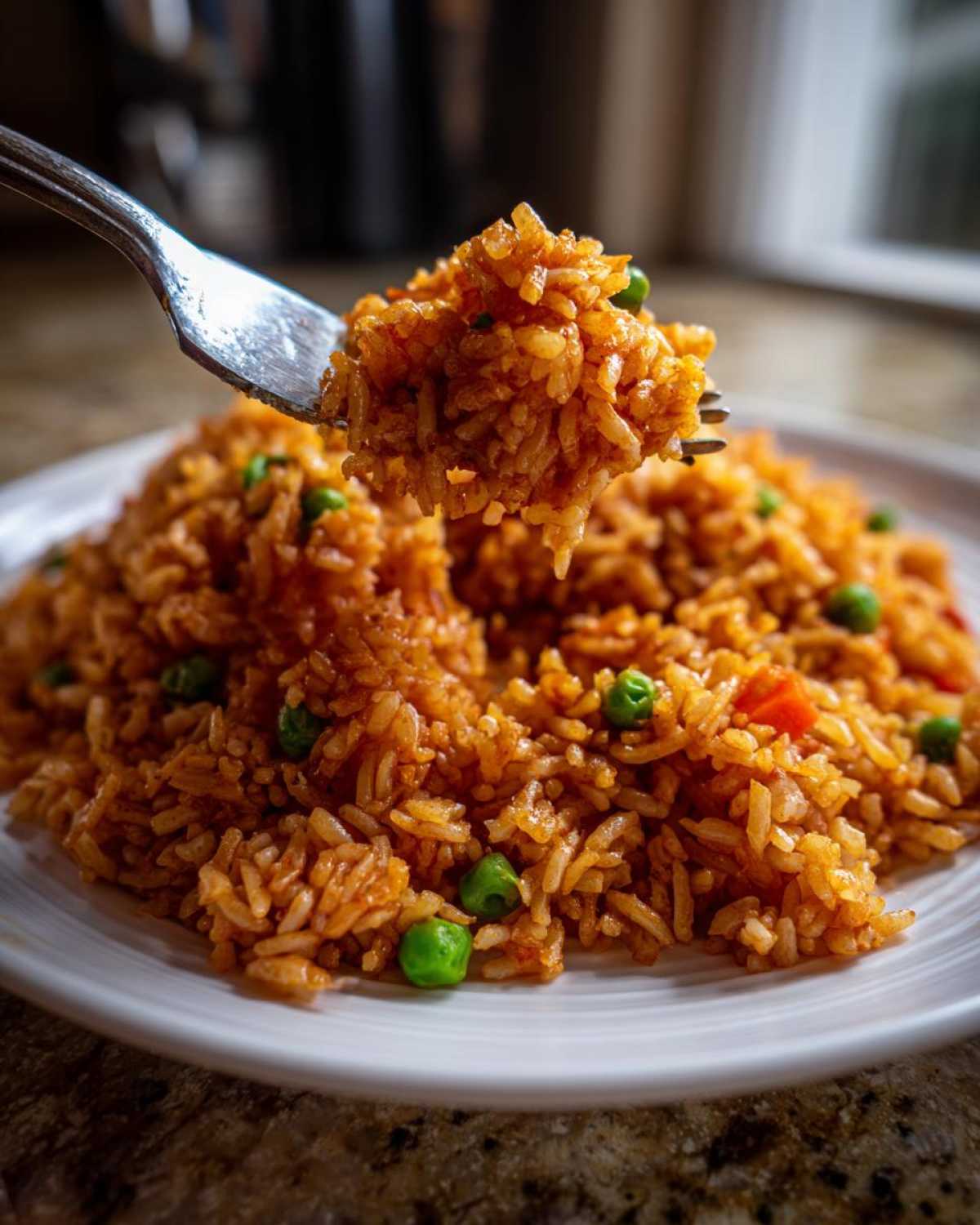 A fork lifting a bite of seasoned, reddish-orange spanish rice mixed with bright green peas from a white plate.