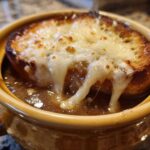 Close-up of a crock of rich french onion soup topped with a thick slice of toasted bread and gooey, melted Gruyère cheese.