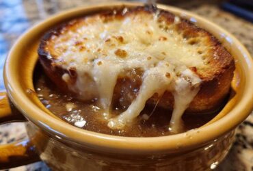 Close-up of a crock of rich french onion soup topped with a thick slice of toasted bread and gooey, melted Gruyère cheese.