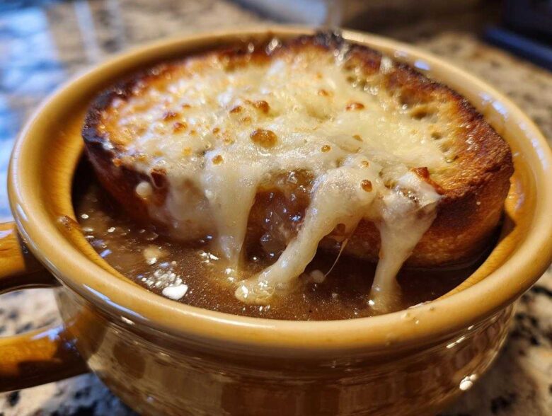 Close-up of a crock of rich french onion soup topped with a thick slice of toasted bread and gooey, melted Gruyère cheese.