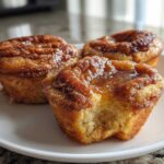 Three delicious french toast muffins on a white plate, one with a bite taken out, showing the soft interior.