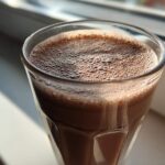 Close-up of a tall glass filled with freshly made chocolate milk, showing a layer of fine foam on top.