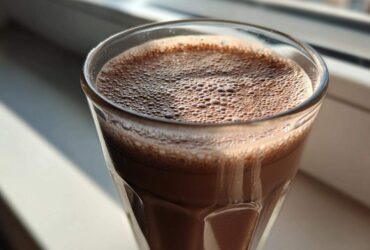 Close-up of a tall glass filled with freshly made chocolate milk, showing a layer of fine foam on top.