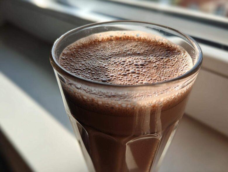 Close-up of a tall glass filled with freshly made chocolate milk, showing a layer of fine foam on top.