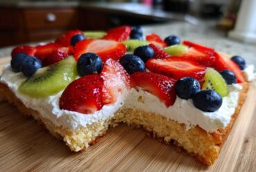 Close-up of a slice of fruit pizza sugar cookie topped with whipped cream, strawberries, blueberries, and kiwi.
