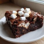 A fudgy square of hot chocolate brownies topped with mini marshmallows on a white plate.