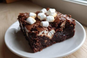 A fudgy square of hot chocolate brownies topped with mini marshmallows on a white plate.