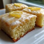 Three squares of fudgy Lemon Brownies topped with white glaze and candied lemon slices on a white plate.
