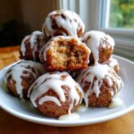 A stack of freshly baked cinnamon roll bites drizzled generously with white icing, one bite is broken open.