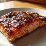 Close-up of a perfectly cooked salmon fillet topped with a thick, shiny, dark glaze.