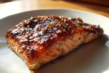 Close-up of a perfectly cooked salmon fillet topped with a thick, shiny, dark glaze.