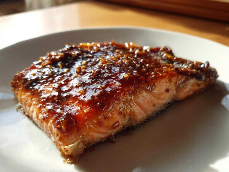 Close-up of a perfectly cooked salmon fillet topped with a thick, shiny, dark glaze.