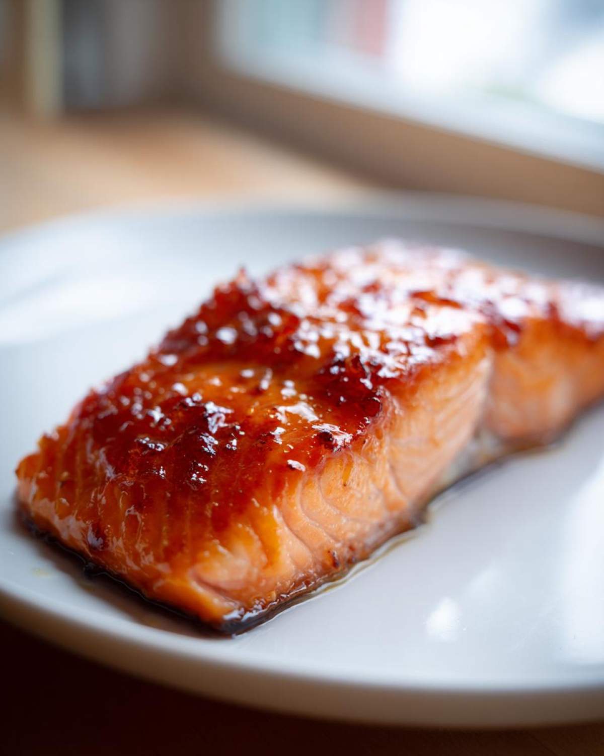 Close-up of a perfectly cooked, glazed salmon fillet resting on a white plate.