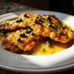 Three golden-brown fillets of chicken piccata swimming in a bright lemon butter sauce and topped with capers and parsley.