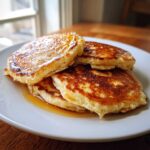 A stack of fluffy discard pancakes glistening with syrup on a white plate.