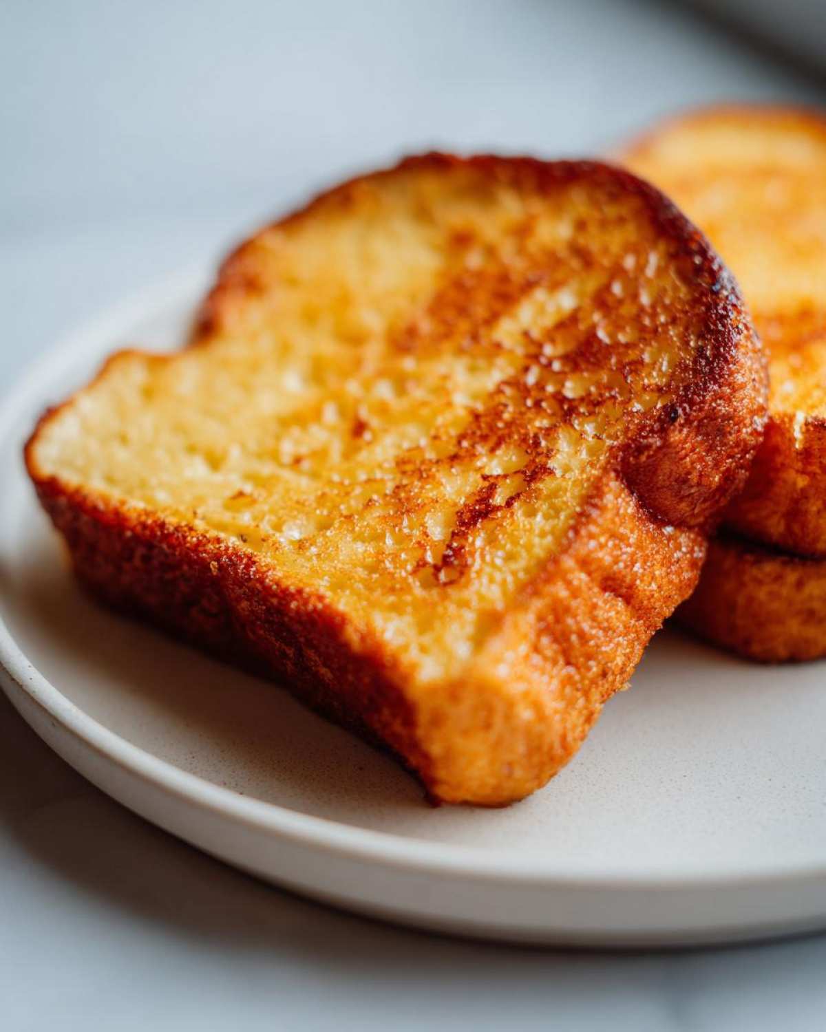 Close-up of golden brown, perfectly cooked slices of easy french toast on a light plate.