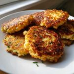 A stack of five golden brown, pan-fried mashed potato cakes garnished with chives.