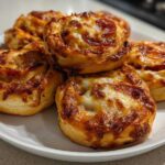 A stack of freshly baked, golden brown pizza pinwheels topped with melted, slightly browned cheese and pepperoni.