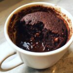 Close-up of a rich, dark chocolate mug cake with a scoop taken out revealing a molten center and chocolate chips.