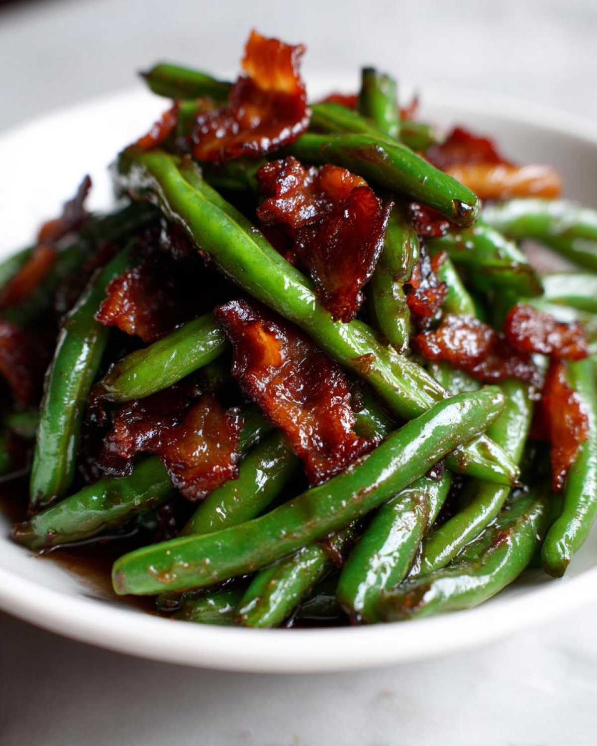 Close-up of glossy, vibrant green beans tossed with caramelized, crispy bacon pieces.