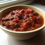 Close-up of a hearty bowl of amazing crockpot chili featuring ground beef, kidney beans, and tomatoes.