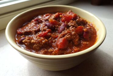 Close-up of a hearty bowl of amazing crockpot chili featuring ground beef, kidney beans, and tomatoes.