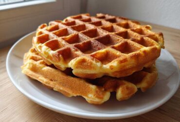 A stack of golden brown, freshly made high protein waffles resting on a white plate.