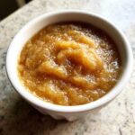 A close-up, top-down view of thick, spiced homemade applesauce served in a small white bowl.