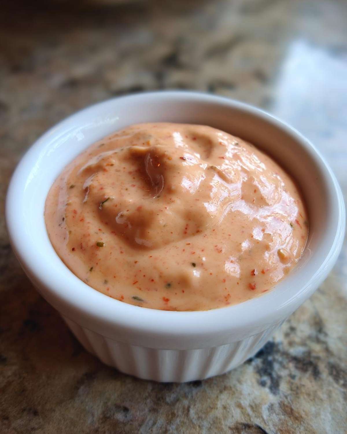 Close-up of creamy, orange-pink homemade big mac sauce speckled with spices in a small white ramekin.