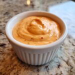 Close-up of creamy, orange-colored big mac sauce with visible spice flecks in a small white ramekin.