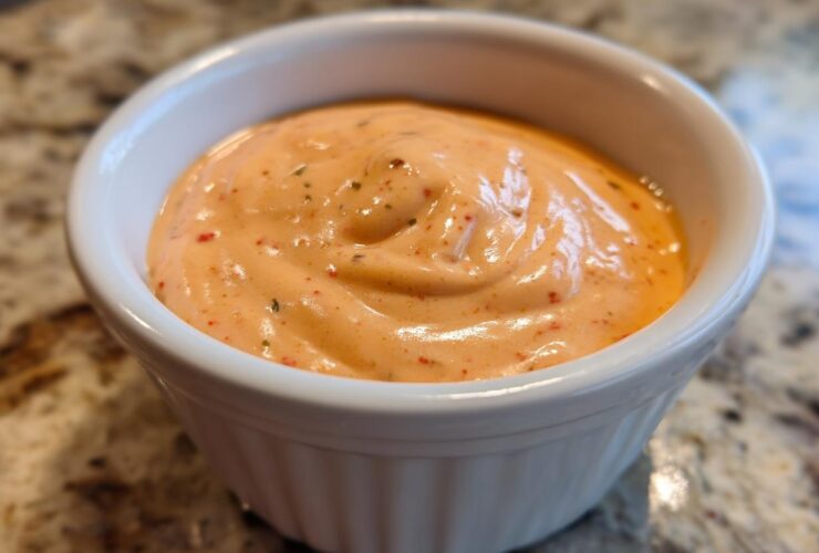 Close-up of creamy, orange-hued big mac sauce speckled with spices, served in a small white dipping bowl.