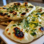 A stack of freshly baked homemade naan bread brushed with melted butter and topped with chopped cilantro.