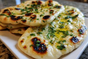 A stack of freshly baked homemade naan bread brushed with melted butter and topped with chopped cilantro.