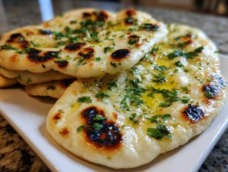 A stack of freshly baked homemade naan bread brushed with melted butter and topped with chopped cilantro.
