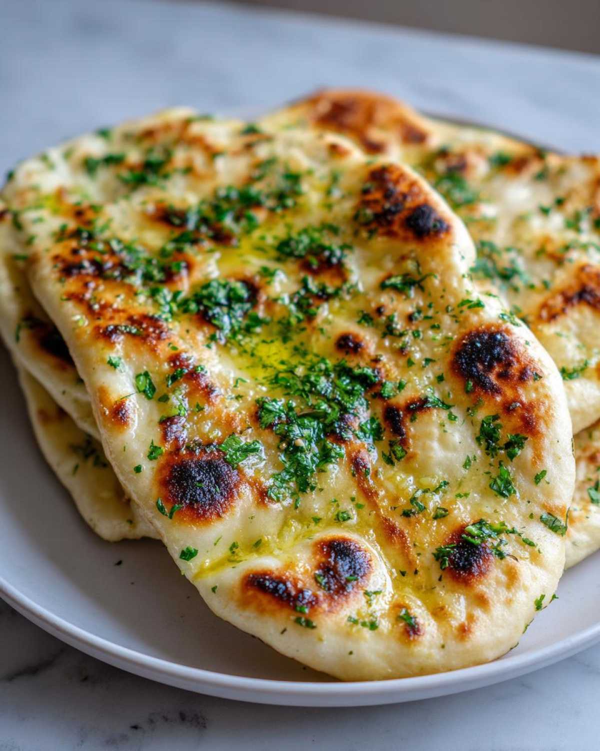 Close-up of warm homemade naan bread brushed with melted butter and sprinkled with fresh green herbs.