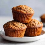 Close-up of three freshly baked honey bran muffins stacked on a white plate.