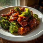 Close-up of glossy, saucy chicken and bright green broccoli florets in a white bowl, featuring honey garlic chicken and broccoli.